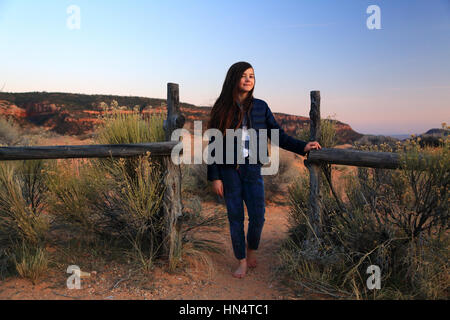 A pretty tween girl stands by a rustic fence in a desert landscape in Coral Pink Sand Dunes State Park in Utah.
