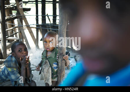 Rural Ugandan poor family in their home, while young children dressed in rags stare at the camera Stock Photo