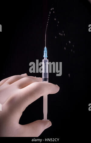 Hand with glove holding the syringe. The contents squirting out of the syringe, isolated on black background Stock Photo