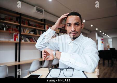Picture of attractive african businessman wearing watch sitting at the table looking at camera. Coworking. Stock Photo