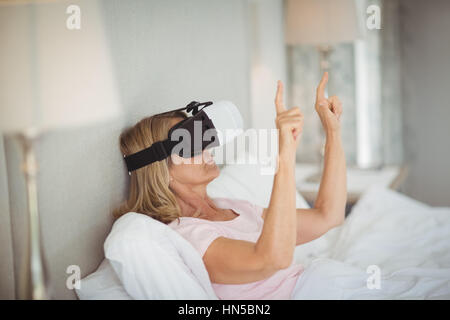 Senior woman lying on bed and using virtual reality headset Stock Photo