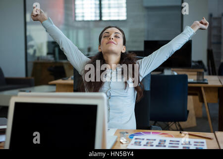 Graphic designer stretching her arms out in office Stock Photo