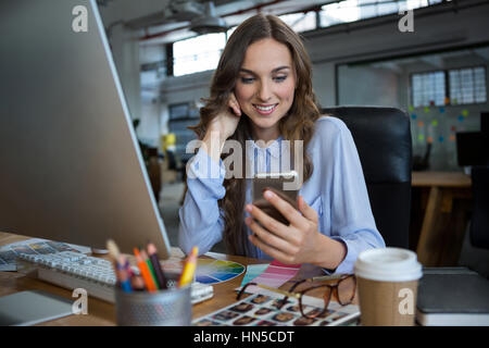 Female graphic designer using mobile phone at desk in office Stock Photo