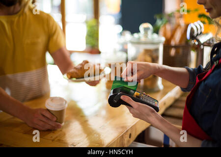 Mid-section of customer making payment through credit card at counter in cafÃƒÂ© Stock Photo
