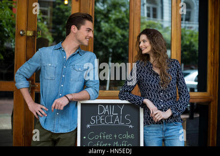 Smiling man and woman leaning on menu board outside the cafe Stock Photo