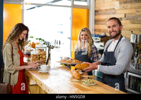 Woman using laptop and waiter cutting bread at counter in cafÃƒÂ© Stock Photo