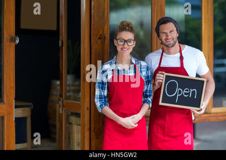 Portrait of smiling waitress and waiter standing with open sign board outside cafÃƒÂ© Stock Photo