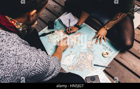 Couple planning vacation using a world map. Man pointing at the map while the woman is making notes in diary. Stock Photo