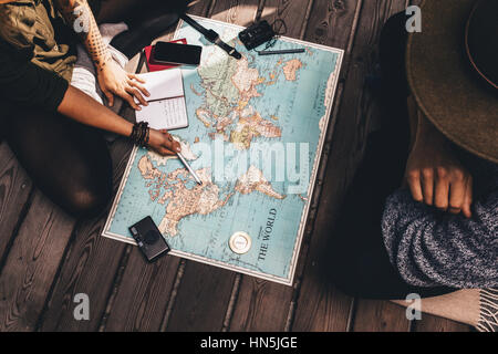 Man and woman discussing tour plans using the world map. Woman making notes and pointing on the map while the man is discussing. Stock Photo