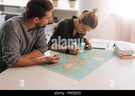 Man and woman studying the world map and taking notes. Woman marking on the world map using pen. Stock Photo