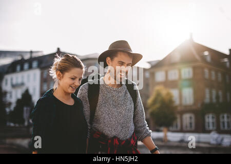 Smiling young couple on vacation walking on street with sunlight in the background. Stock Photo