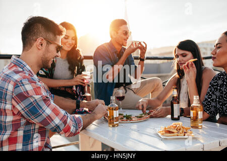 Group of young people sitting around and eating pizza. Friends partying and eating pizza. Stock Photo