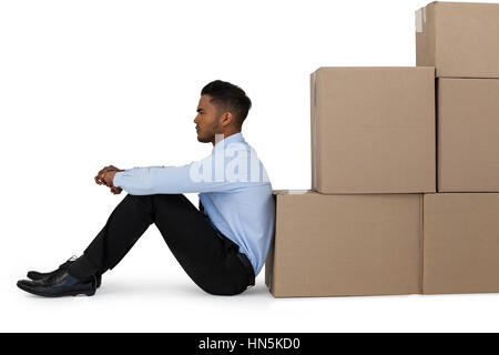 Thoughtful businessman leaning on cardboard boxes against white background Stock Photo