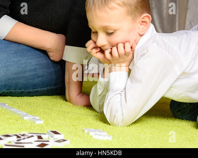 child with his mother playing dominoes lying on the carpet Stock Photo