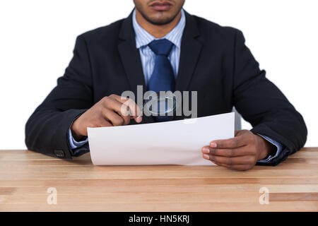 Mid section of businessman looking at document through magnifying glass Stock Photo