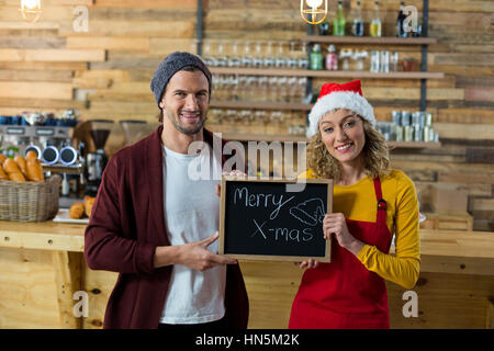 Portrait of smiling waitress and owner standing with merry x mas sign board in cafe Stock Photo