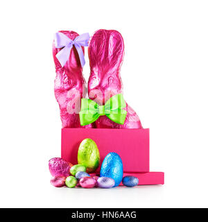 Gift box with chocolate easter eggs, couple of rabbits with bow, wrapped in pink foil and colorful candies isolated on white background clipping path  Stock Photo