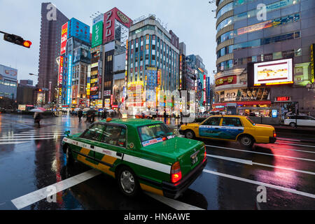 Tokyo, Japan - March 2, 2012: On a rainy evening, two Tokyo taxis wait at a road junction on Yasukuni Dori in Shinjuku, with colourfully lit buildings Stock Photo