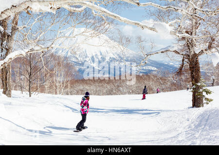 NISEKO, JAPAN - MARCH 10 : General view of people snowboarding on a tree-lined piste in the Niseko Grand Hirafu ski resort, Hokkaido, Japan on 10th Ma Stock Photo