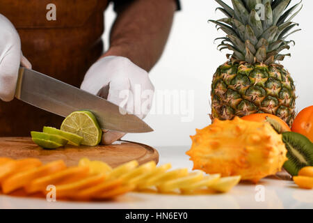 Man in white gloves cutting a slice of lime in pieces; collection of tropical fruits Stock Photo