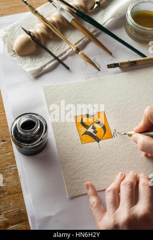 Calligraphy studio, hand writing text with pen and nib, letter S coated with gold on torchon paper Stock Photo