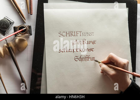 Calligraphy studio, hand writes text with ink, pen and nib, Gothic script on Ingres paper, inkwell and pen holder at back Stock Photo