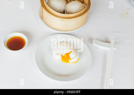 Dim sum food Steamed lava bun in bamboo basket at restaurant with soy sauce, sweet sauce, chili sauce and chopsticks. Stock Photo