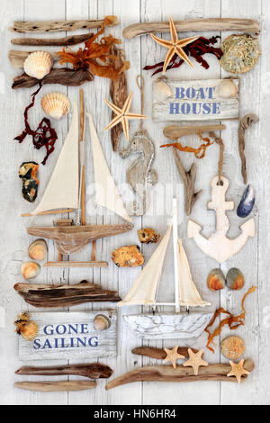 Marine and nautical themed  abstract with decorative sailing boats, signs, seashells, driftwood, seaweed and rocks on distressed white wood background. Stock Photo
