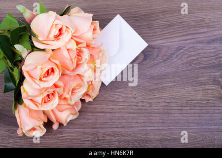 Beautiful roses with a note in the envelope on a wooden base Stock Photo