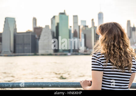 Young woman in striped shirt looking at New York City skyline during sunset Stock Photo