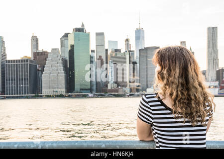 Young woman in striped shirt looking at New York City skyline during sunset Stock Photo