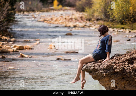 White water Mineral Creek stream in Colorado, USA during the fall with golden aspens and woman on edge dipping feet in water Stock Photo