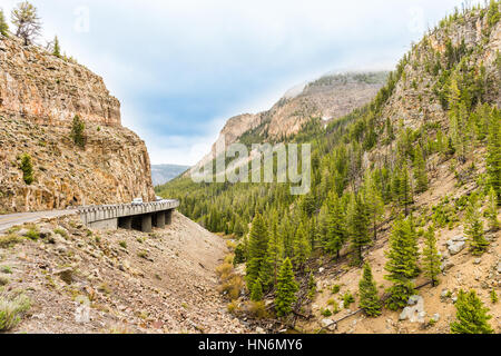 Sharp turn on curvy road in rocky canyon mountain in Yellowstone National Park with cars Stock Photo