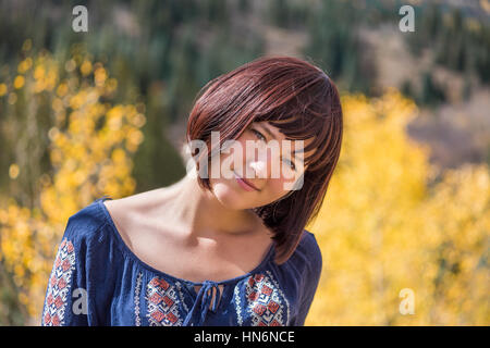 Portrait of young happy smiling woman with purple plum hair by autumn aspen trees with head tilted Stock Photo