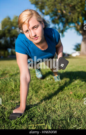 Young woman performing dumbbell row exercise lifting 12 pound weight in green grass outdoor park Stock Photo