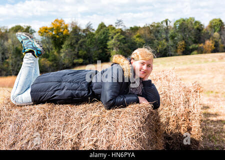 Young woman lying down on hay roll bale Stock Photo