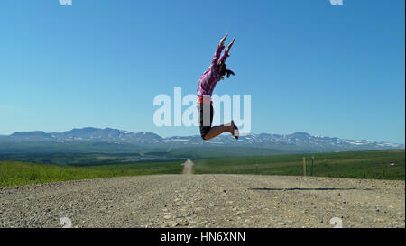 Woman jumping in the air on empty and unsealed Dempster highway in Canada Stock Photo