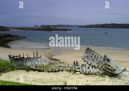 An old wrecked wooden boat on the shore of Highland  in Scotland with the floating boats on the sea at the background.