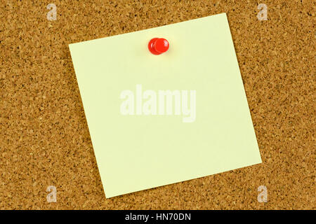 Blank yellow sticky note held on a cork notice board with a red pushpin. Stock Photo