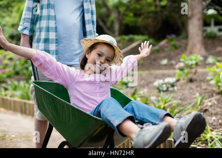 Father pushing daughter in wheelbarrow at park Stock Photo
