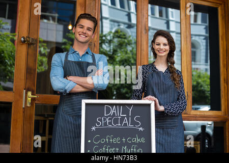 Smiling waiter and waitress standing with menu board outside the cafe Stock Photo