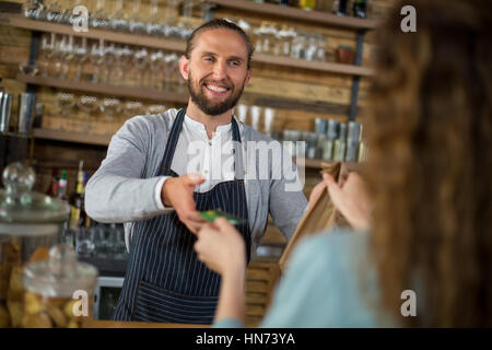 Customer giving credit card to waitress while receiving parcel at counter in cafÃƒÂ© Stock Photo