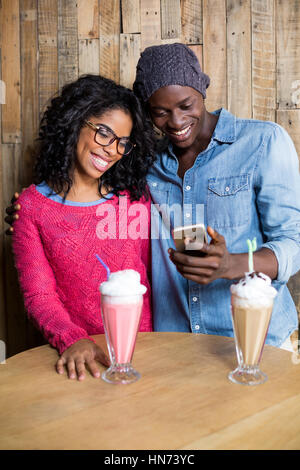 Smiling couple using mobile phone against wooden background in cafÃƒÂ© Stock Photo