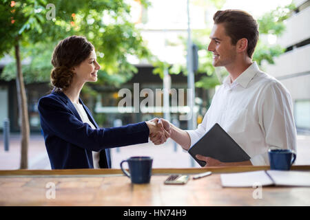 Businesswoman shaking hands with businessman at counter in cafe Stock Photo