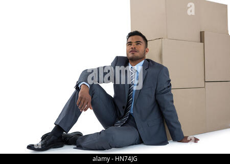 Thoughtful businessman leaning on cardboard boxes against white background Stock Photo