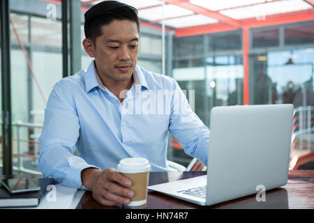 Businessman using laptop while having coffee in office Stock Photo