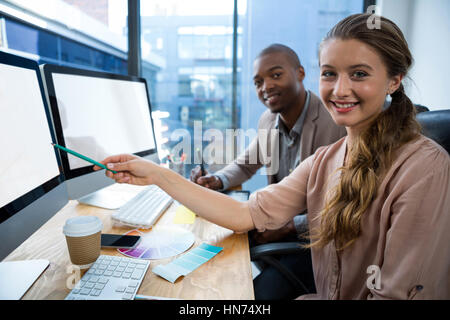 Portrait of graphic designer at desk with colleague in office