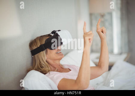 Senior woman lying on bed and using virtual reality headset Stock Photo