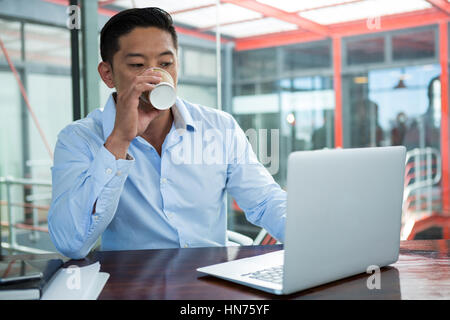Businessman drinking coffee while working on laptop in office Stock Photo
