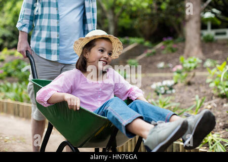 Father pushing daughter in wheelbarrow at park Stock Photo